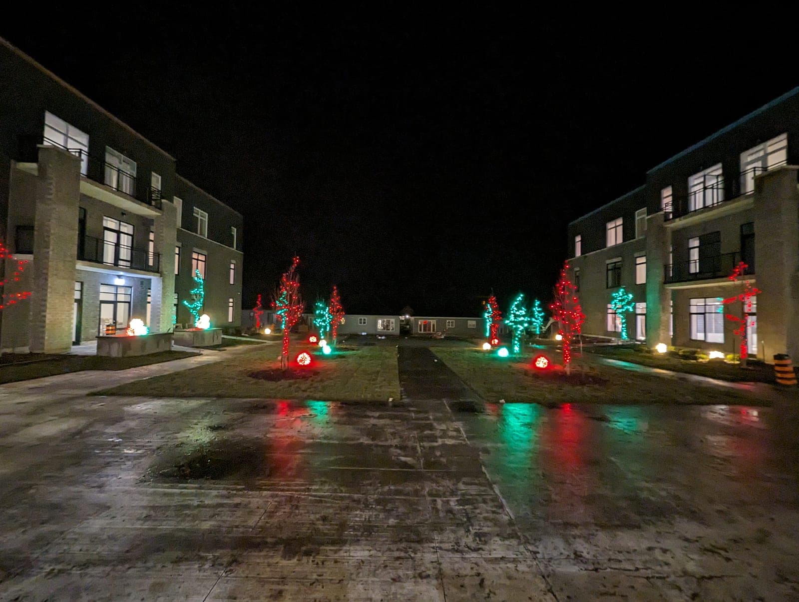 Apartment complex courtyard framed by red and green lit Christmas trees and warm-white roofline accent lighting