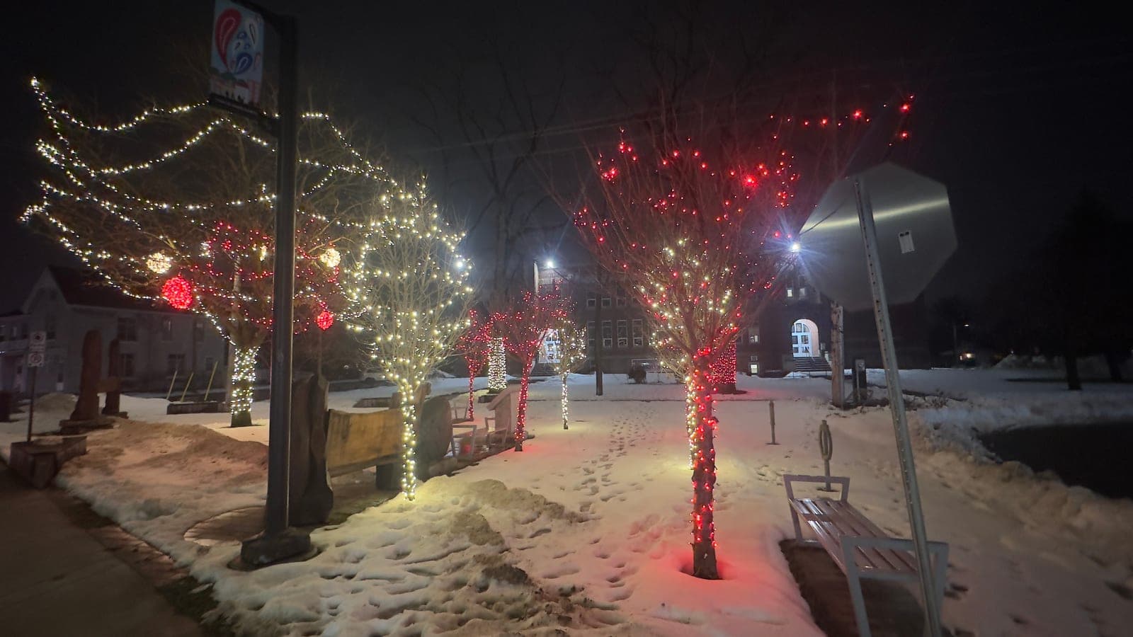 Downtown main street decorated with pole banners and warm white string lighting across the road for a municipal holiday program