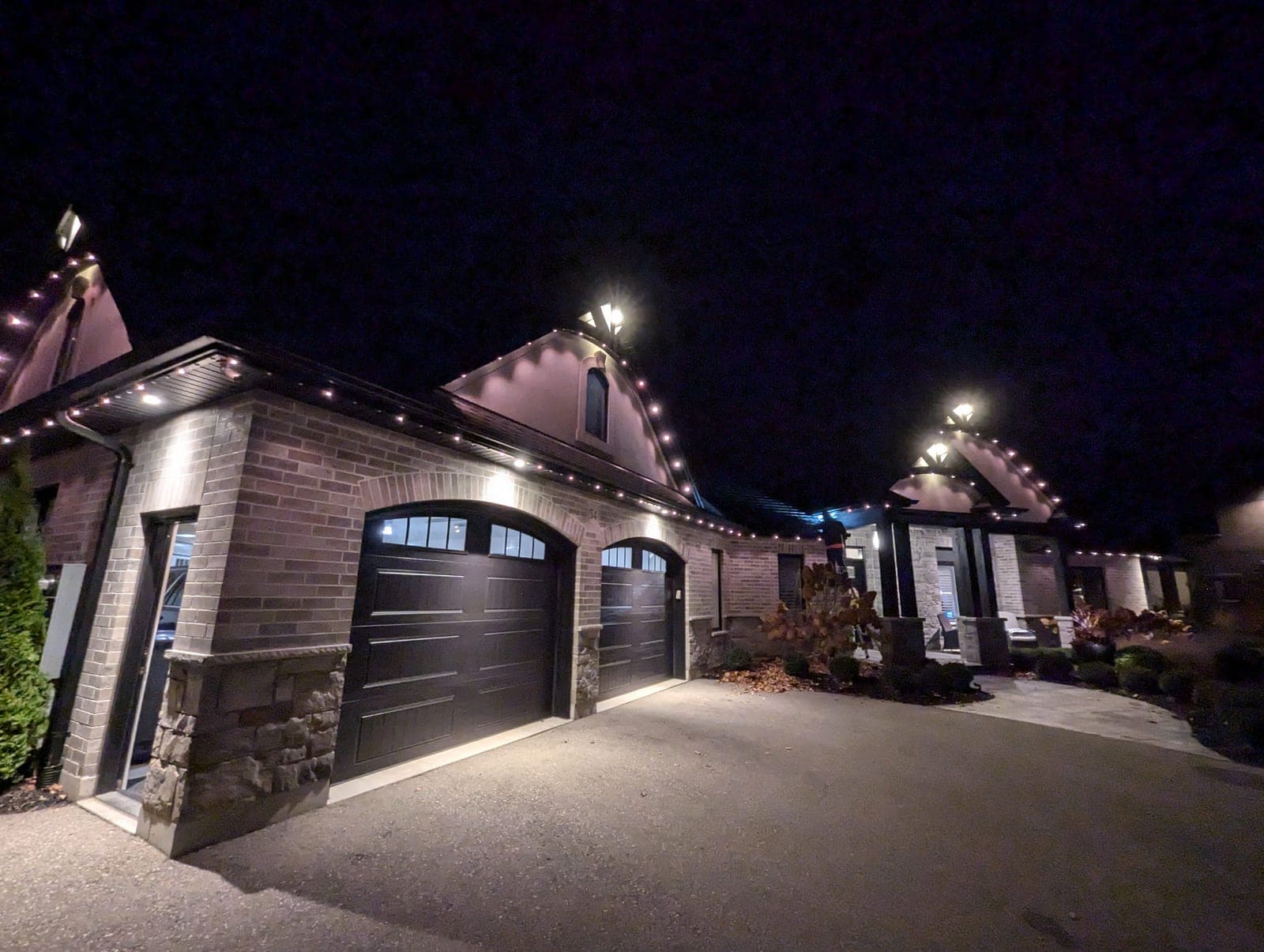 Upscale brick home with warm-white C9 roofline Christmas lights along the eaves and peaks