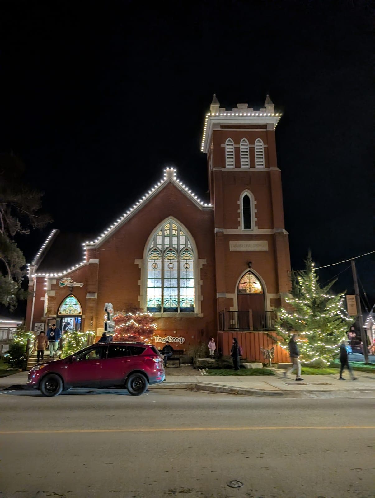Historic red-brick church outlined in warm-white roofline lights with an illuminated evergreen tree at night
